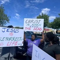 Church members holding Christ is Risen and Jesus is Resurrection and Life signs during an Easter street outreach