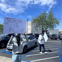 Two church members holding a Jesus is Alive sign in a parking lot