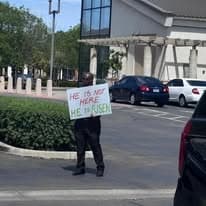 Church member holding a He is Not Here, He is Risen sign near a building