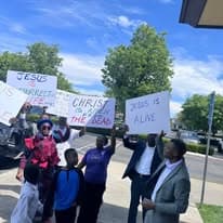 Group holding Jesus is Alive and Christ is Risen signs outdoors